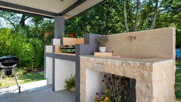 An outdoor kitchen area with a stone fireplace, a grill, and various potted plants.