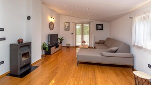 A modern living room with a grey sofa, wooden flooring, a TV, a fireplace, and a large window with curtains.