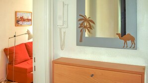 A room with a wooden dresser, a red sofa, a lamp, a wall-mounted telephone, and a mirror with a camel silhouette. - 1 bedroom beautiful apartment in Wismar (Wismar)