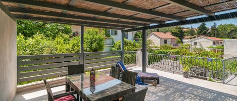 A covered outdoor area with a table and chairs, a railing, and a view of houses and greenery.