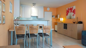Une cuisine moderne avec des meubles blancs, un coin repas avec des chaises en bois et un îlot central.