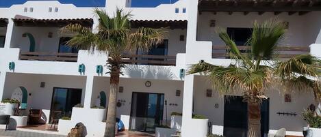 A white building with multiple balconies, palm trees, and outdoor seating areas.