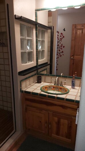 A bathroom with a tiled sink, wooden cabinets, a mirror, and a window with blinds. - Villa 8 A Great Place to Relax and Create Great Memories! (Puerto Peñasco)