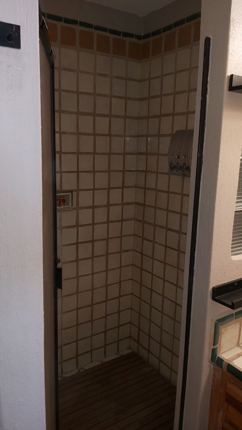 Une douche d’angle avec un mur carrelé et un sol en bois.