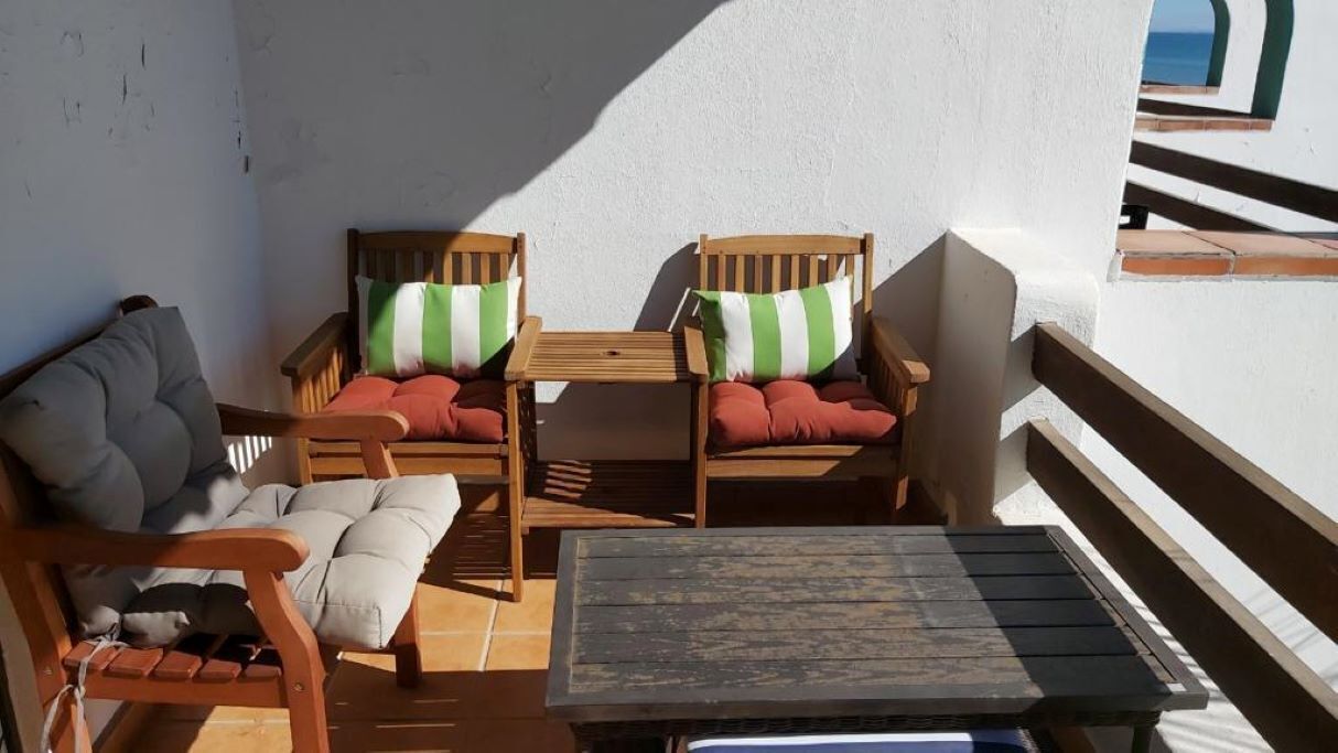 Ein Balkon mit Holzmöbeln, darunter zwei Stühle mit Kissen und ein kleiner Tisch.