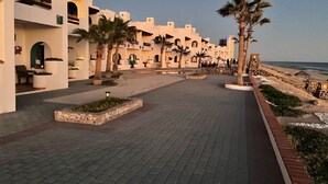 A courtyard with white buildings, palm trees, and a paved walkway leading to the beach. - Villa 8 A Great Place to Relax and Create Great Memories! (Puerto Peñasco)
