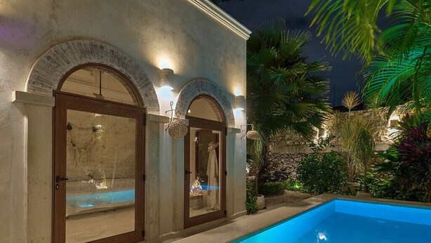 A swimming pool with a stone wall and arched doorways, surrounded by tropical plants. - Luxury Casa Lourdes in Merida, Centro (Mérida)