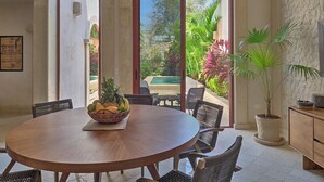 A dining area with a round wooden table, wicker chairs, and a fruit basket. - Luxury Casa Lourdes in Merida, Centro (Mérida)