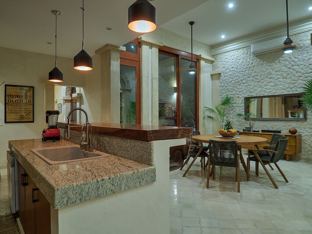 A kitchen with granite countertops, a dining area with a round table and chairs, pendant lighting, and a stone-textured wall.