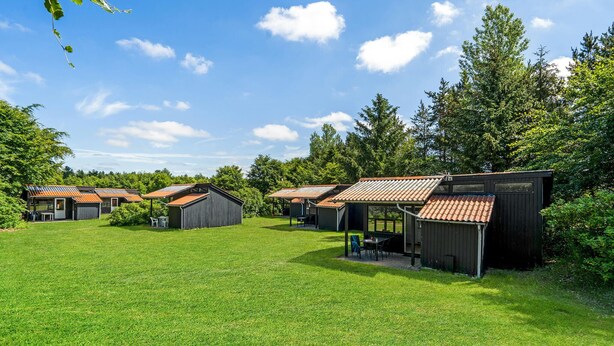 A row of small, rustic cabins with sloped roofs, surrounded by a lush green lawn and dense trees. - Amazing home in Hampen with WiFi (Hampen)