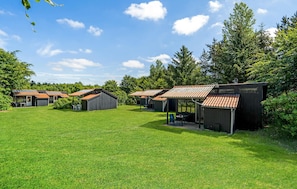 A row of small, rustic cabins with sloped roofs, surrounded by a lush green lawn and dense trees.