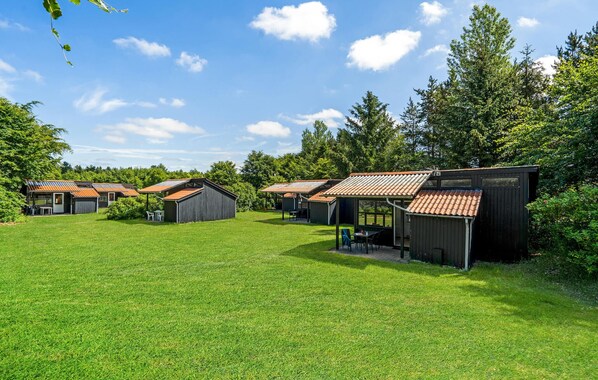 A row of small, rustic cabins with sloped roofs, surrounded by a lush green lawn and dense trees.