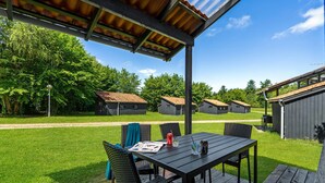 A covered outdoor seating area with a table and chairs, surrounded by a grassy lawn and small buildings in the background. - Amazing home in Hampen with WiFi (Hampen)