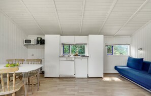 A compact kitchen with white cabinets, a microwave, and a coffee maker. There is a dining table with chairs and a blue sofa in the living area.