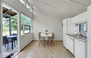 A kitchen with a white interior, a dining table with chairs, and a view of the outdoors through large windows.