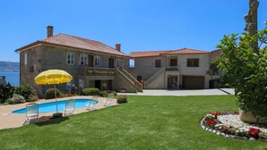 Una casa de piedra de dos pisos con piscina, zona de estar exterior y vista al mar.