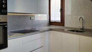 Cocina con armarios blancos, encimera de granito, horno empotrado y ventana con cortina.