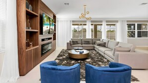 A modern living room with a sectional sofa, a round coffee table, and a wooden entertainment unit. - 9BR house with game room near Disney area (Kissimmee)