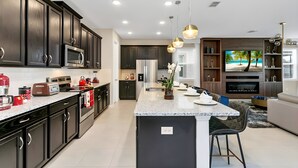 A modern kitchen with dark cabinetry, a central island, and a dining area with a TV and seating. - 9BR house with game room near Disney area (Kissimmee)