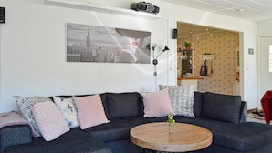 A modern living room with a dark grey sectional sofa, a round wooden coffee table, and a cityscape artwork on the wall. - 4 bedroom nice home in Trosa (Trosa)