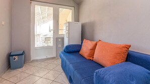 En kompakt opholdsstue med en blå sofa, en orange pude, et hvidt køleskab og en skraldespand.
