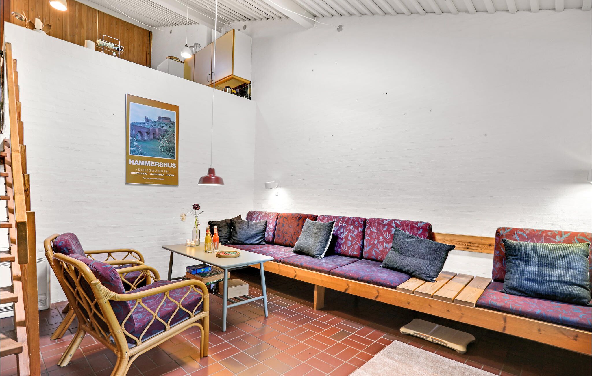 Een gezellige zithoek met een bank, stoelen, een tafel en een poster aan de muur.