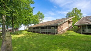 Eine rustikale Holzhütte mit überdachter Veranda und Ziegelaußenwand, umgeben von üppiger Vegetation und Bäumen.
