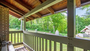 Eine Holzterrasse mit Geländer, eine Ziegelmauer und Blick auf eine bewaldete Landschaft mit Felsen und einer Holzhütte.