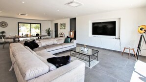 A modern living room with a large sectional sofa, a glass coffee table, and a flat-screen TV mounted on the wall.