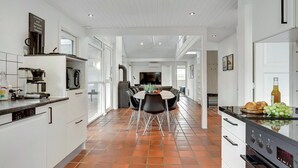 Een moderne keuken met een eethoek, met een koffieapparaat, een grote televisie en een betegelde vloer.