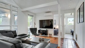 Een moderne woonkamer met een leren bank, een salontafel en een flatscreen televisie. Een groot raam zorgt voor natuurlijk licht en uitzicht.