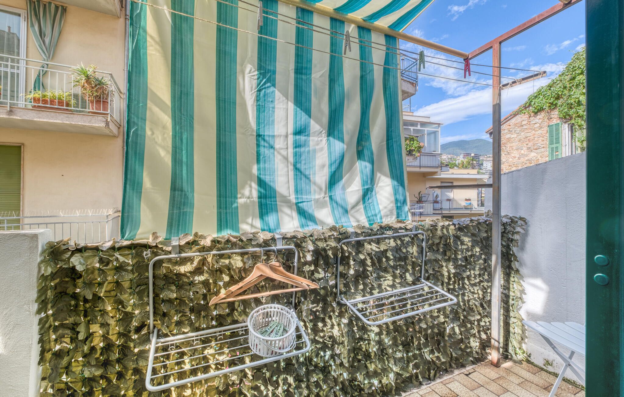 A balcony with a striped awning, a metal drying rack, and a stone wall.