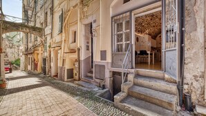 Une rue étroite, bordée de bâtiments des deux côtés, avec une porte bien visible et un escalier menant à un deuxième étage.