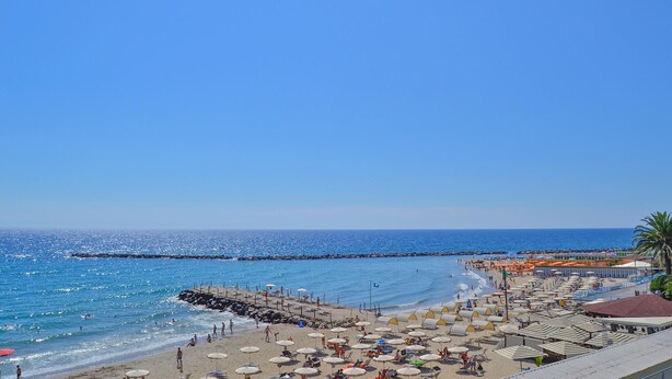 Une plage avec des parasols et des chaises longues, une jetée et un ciel bleu dégagé.