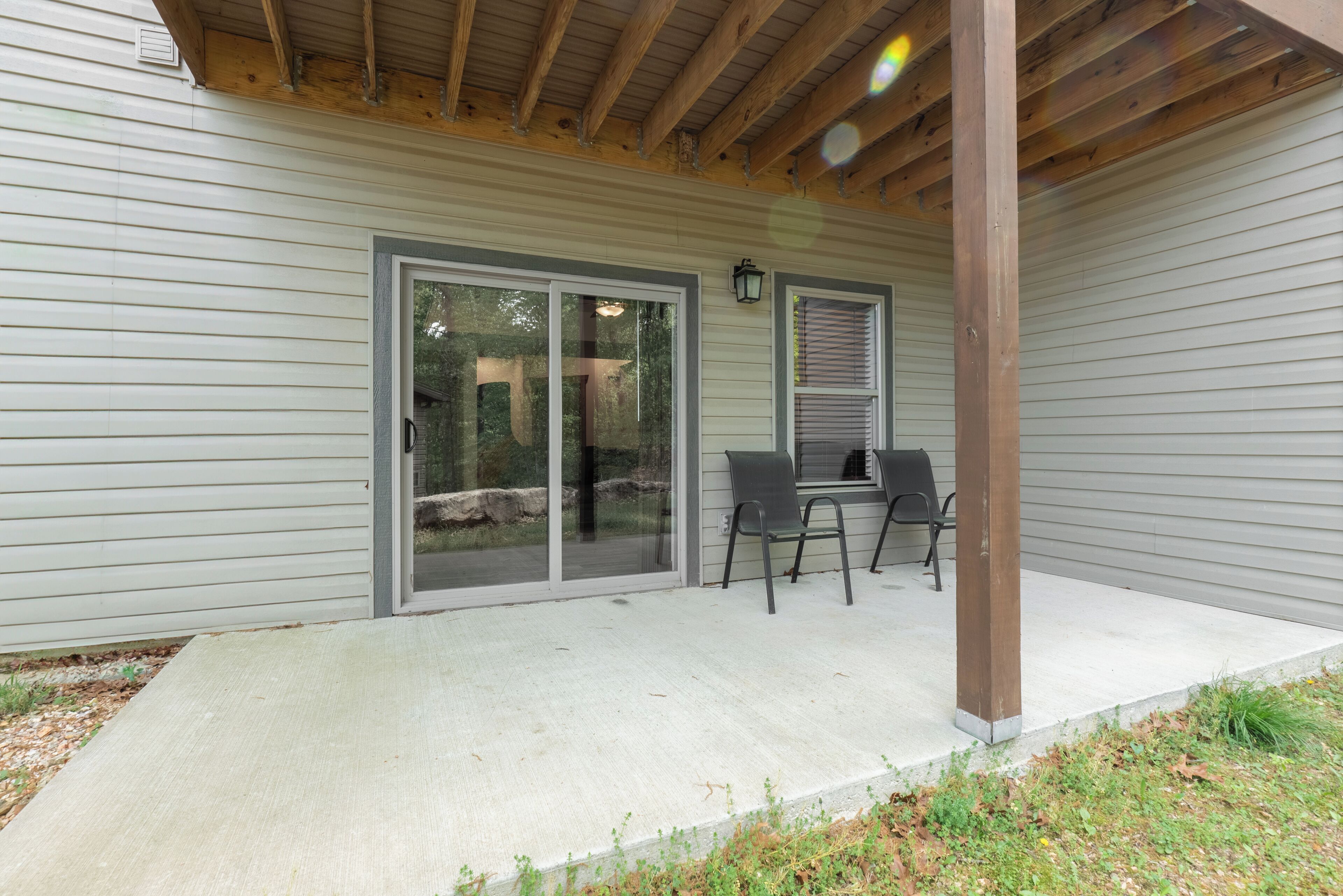 A covered patio with a concrete floor, two chairs, and a wooden beam structure.