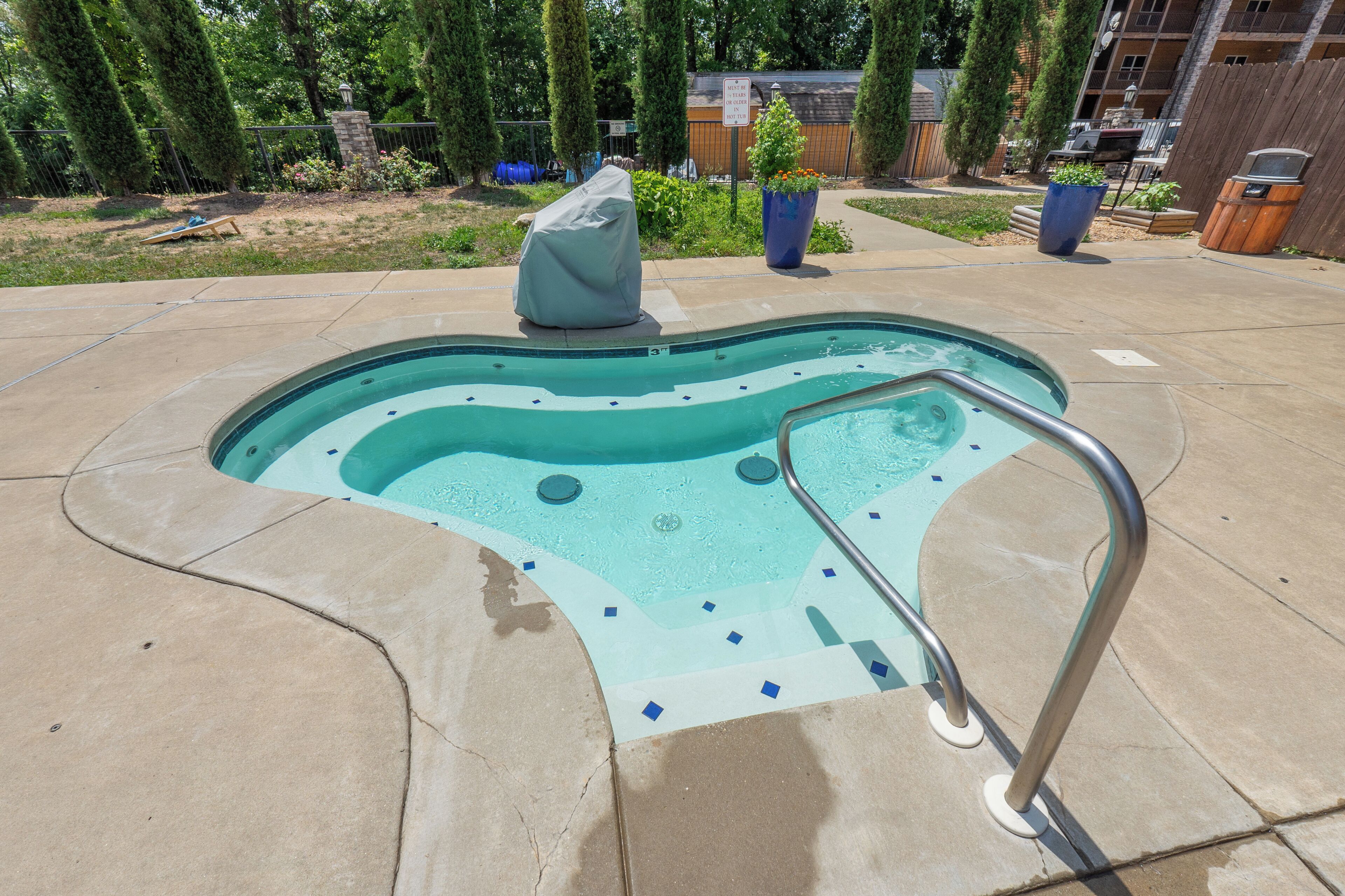 Een hottub met een metalen trap, omringd door een betonnen terras en een houten omheining.