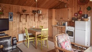 A cozy cabin-style kitchen with wooden walls, a dining table with chairs, a television, and a refrigerator.