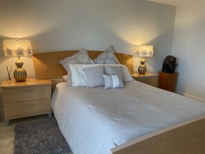 A neatly made bed with white linens, two bedside tables with lamps, and a wooden headboard.