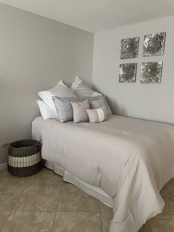 A neatly made bed with a light-colored duvet and several pillows, a wicker basket, and four metallic wall art pieces. - Penthouse Condo, with stunning ocean views (Surfside)