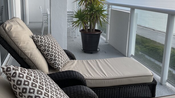 En balkon med sofa, mønstrede puder, en potteplante og havudsigt.