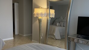 Et hotelværelse med en seng, et skrivebord med et fjernsyn, en lampe og et spejl der viser rummet.