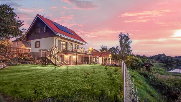 Uma casa de dois andares com telhado vermelho, base de pedra e gramado bem cuidado.
