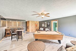 Relax in a spacious room with a pool table and comfortable seating area, featuring a ceiling fan for ventilation and a door leading to another space.