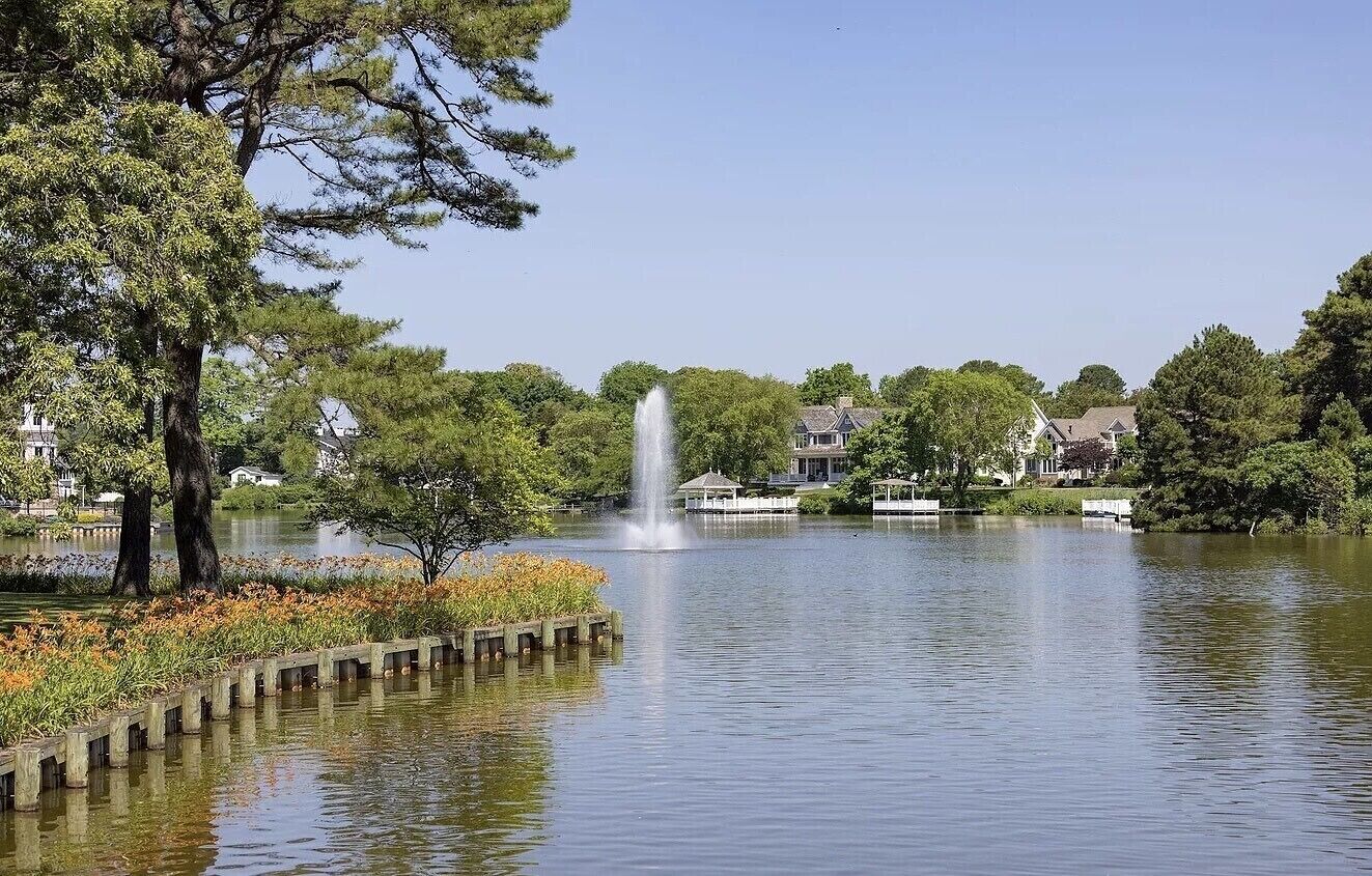 Un lac paisible avec une fontaine, entouré d’arbres et de maisons.