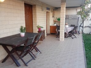 Ein überdachter Patio-Bereich mit Tisch und Stühlen, einem Holzschrank und einem Blumentopf.