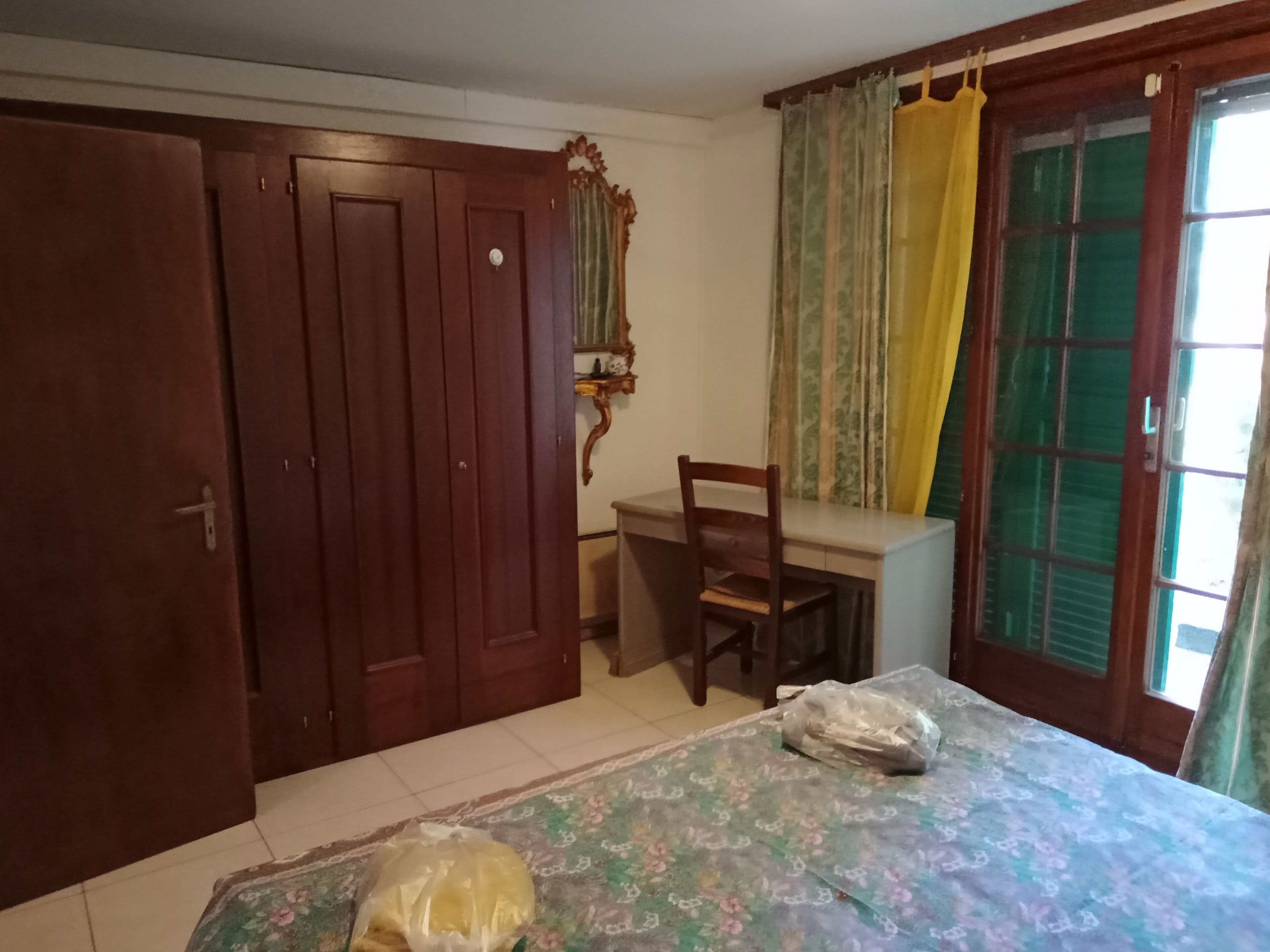 Ein Schlafzimmer mit Bett, Schreibtisch, Stuhl, Kleiderschrank und einem Fenster mit Vorhängen.