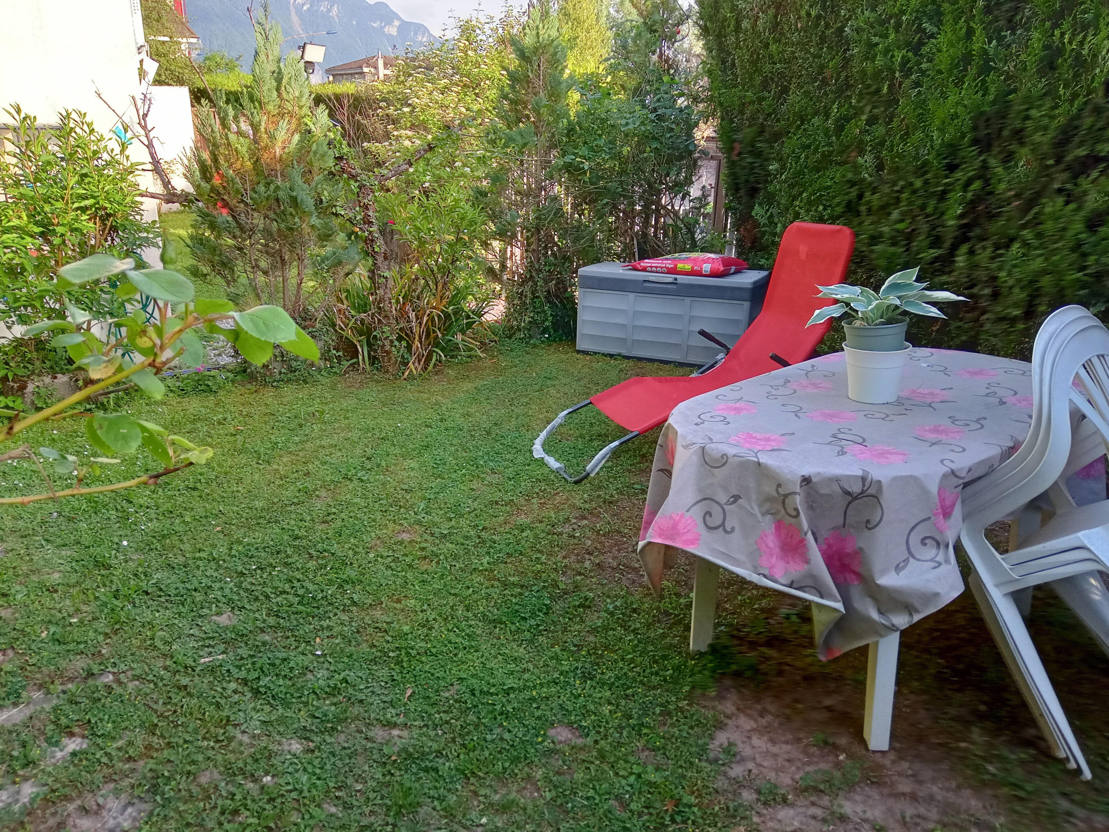 Ein kleiner Sitzbereich im Freien mit Tisch und Stühlen, umgeben von Grünpflanzen und Blick auf Berge.