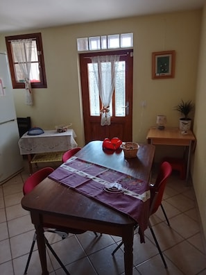 A dining area with a wooden table, red chairs, a purple tablecloth, and a window with lace curtains. - Apartment with garden 100mt from Lake Geneva (Clarens)