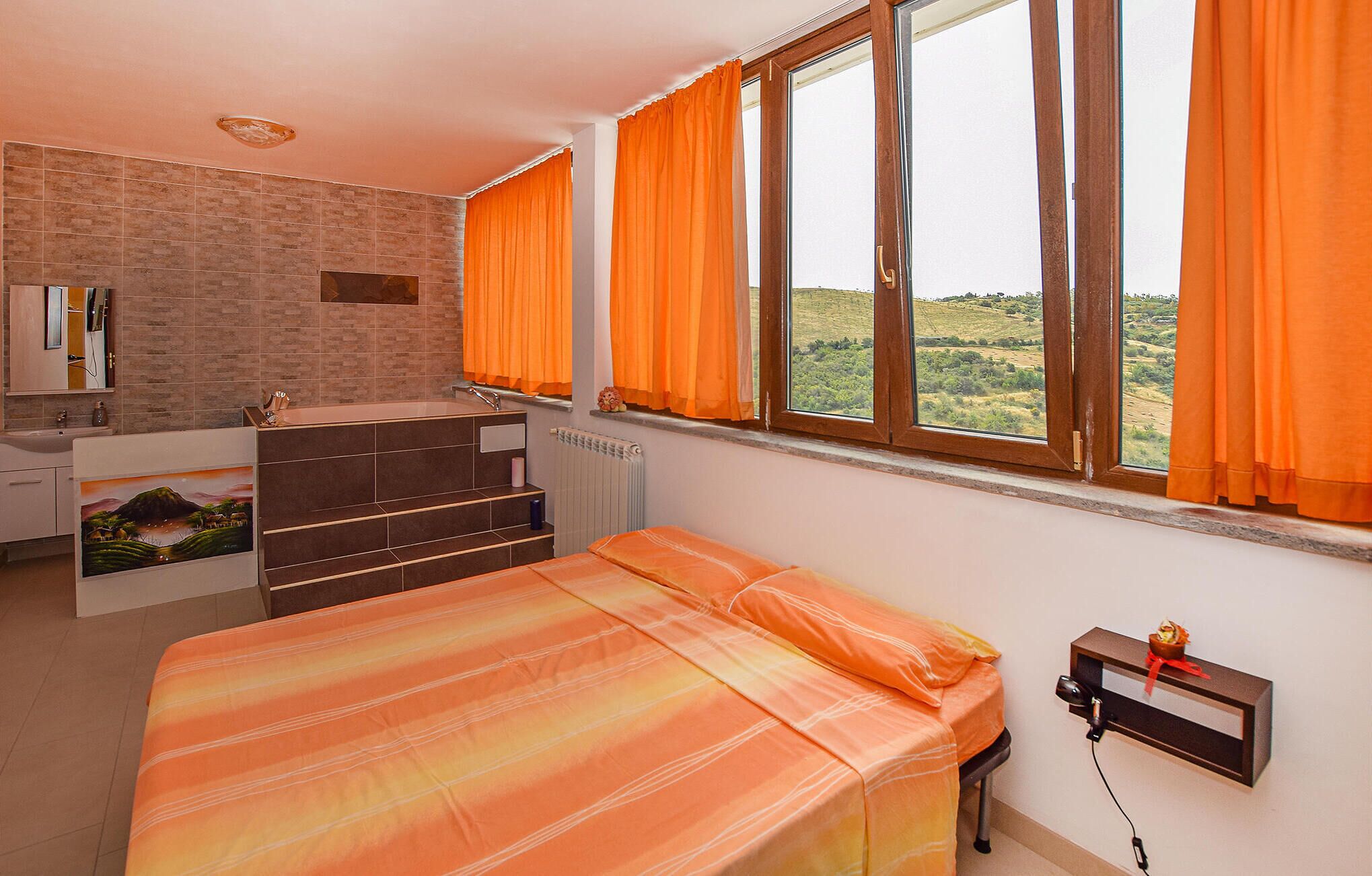 Une chambre avec un lit, une salle de bain avec une baignoire et une fenêtre avec des rideaux.