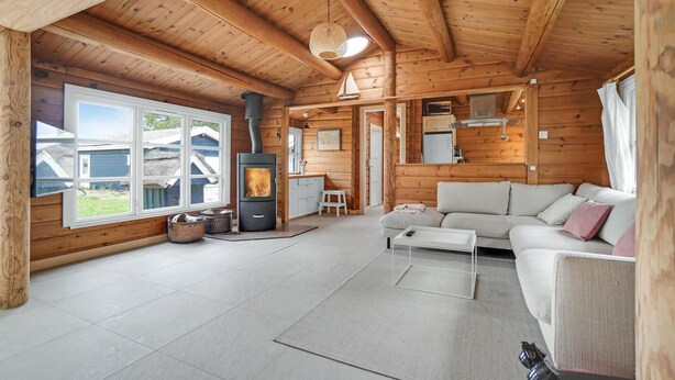 A cozy cabin interior with a large window, a fireplace, a sofa, and a dining area. - Stunning home in Skibby with WiFi (Skibby)